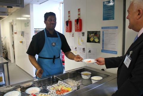 Person in apron serving food in cafeteria