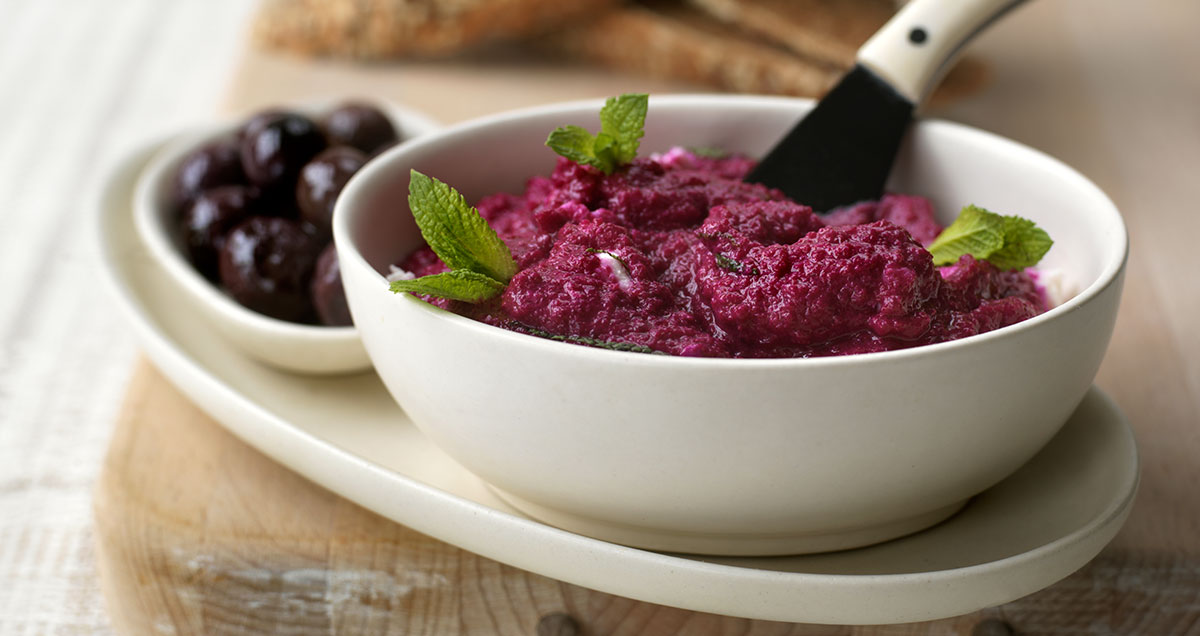 A bowl of beetroot dip with a side of olives