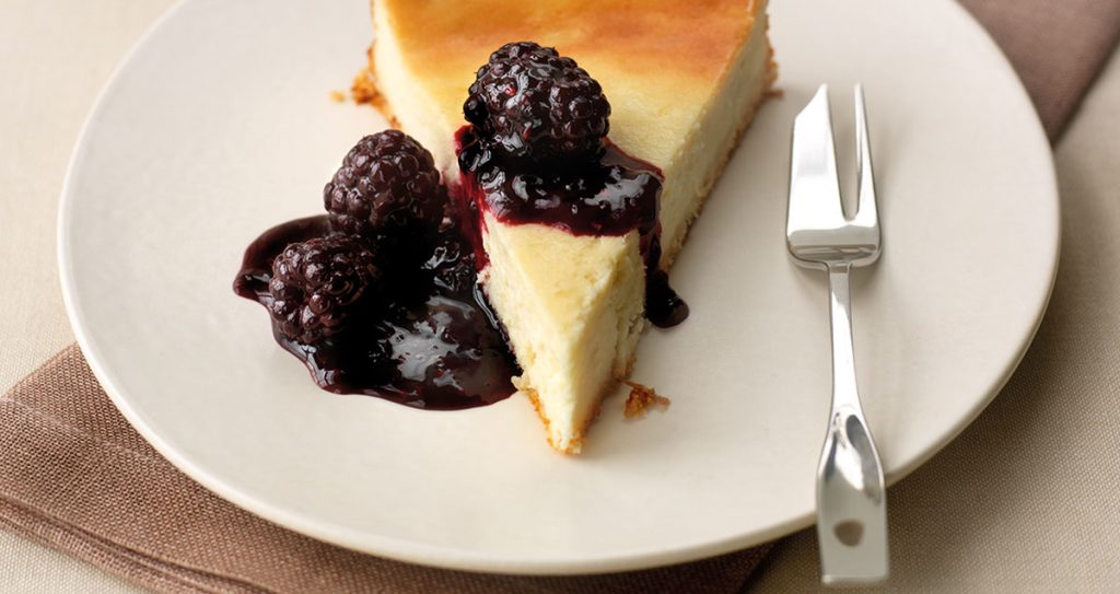A slice of New York baked lemon cheesecake with blackberry compote
