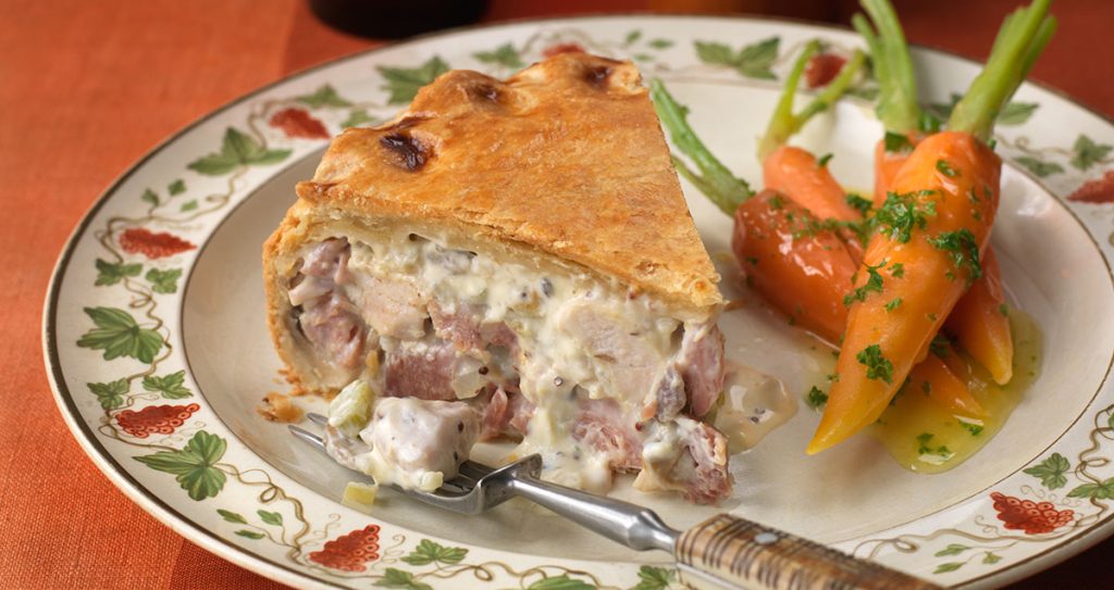 A slice of chicken and ham pie on a plate with cooked whole carrots