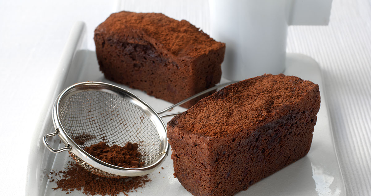 Two chocolate loaves on a platter with a sieve filled with cocoa in between