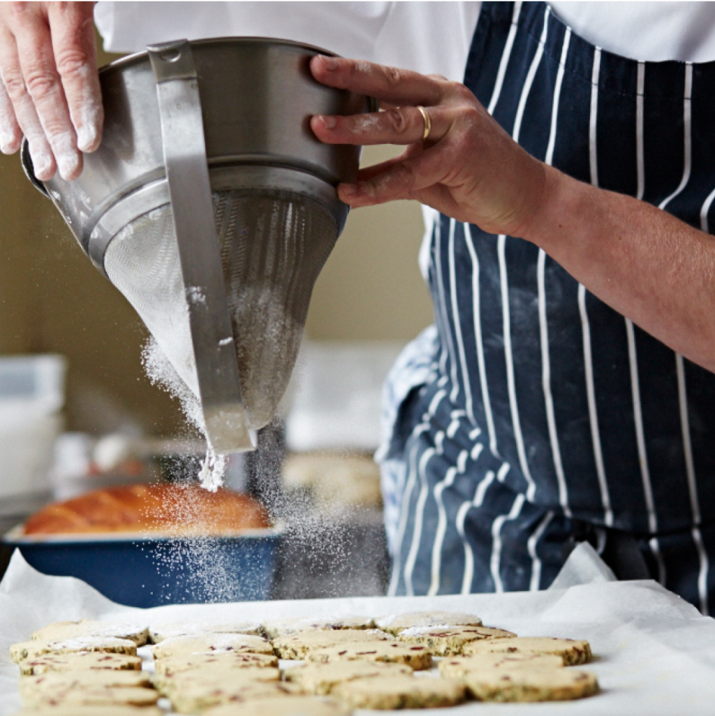 close-up of chef in uniform sieving flour over cookies on tray